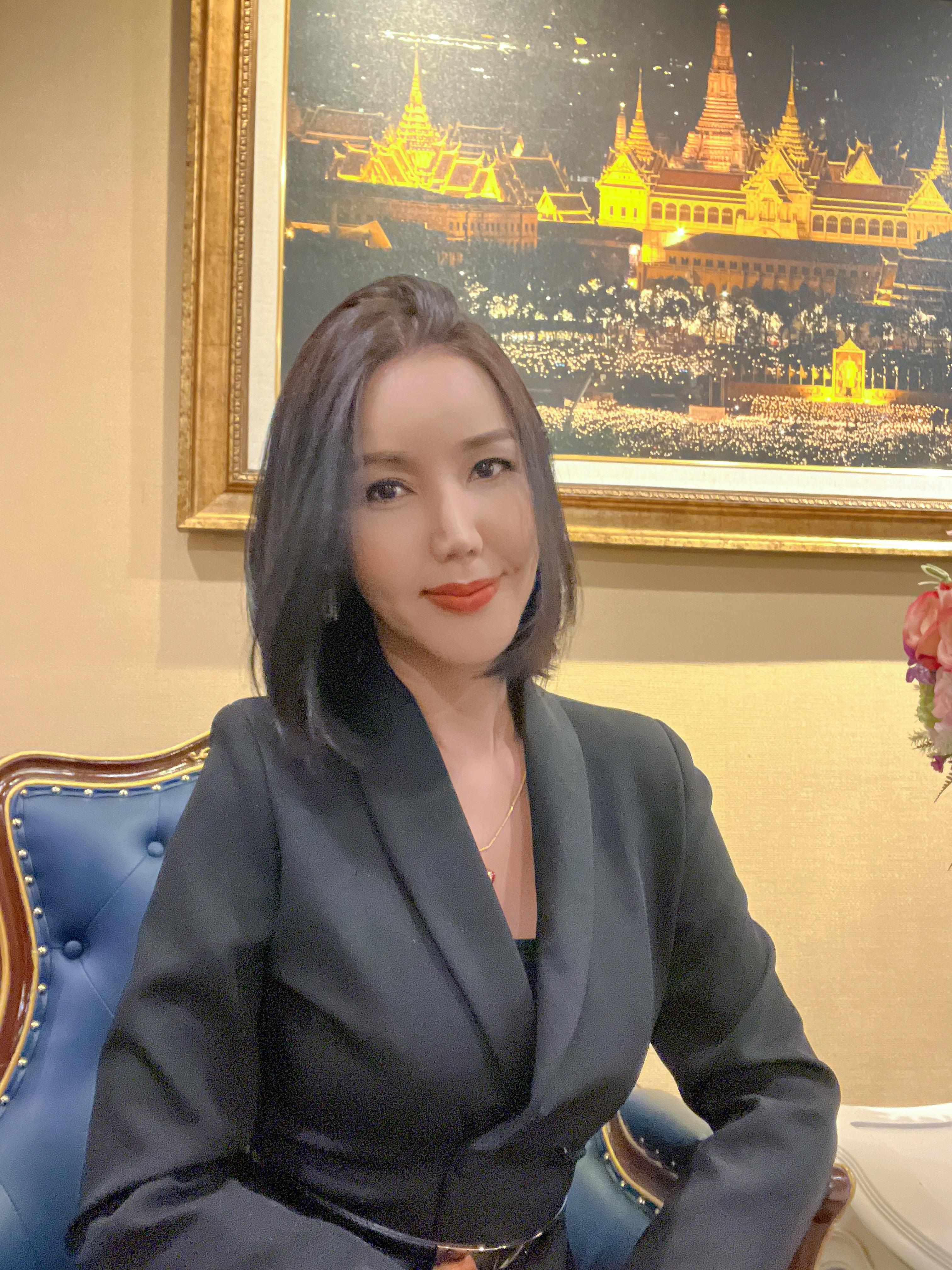 Formal portrait of Chanya with a Thai architectural painting behind her